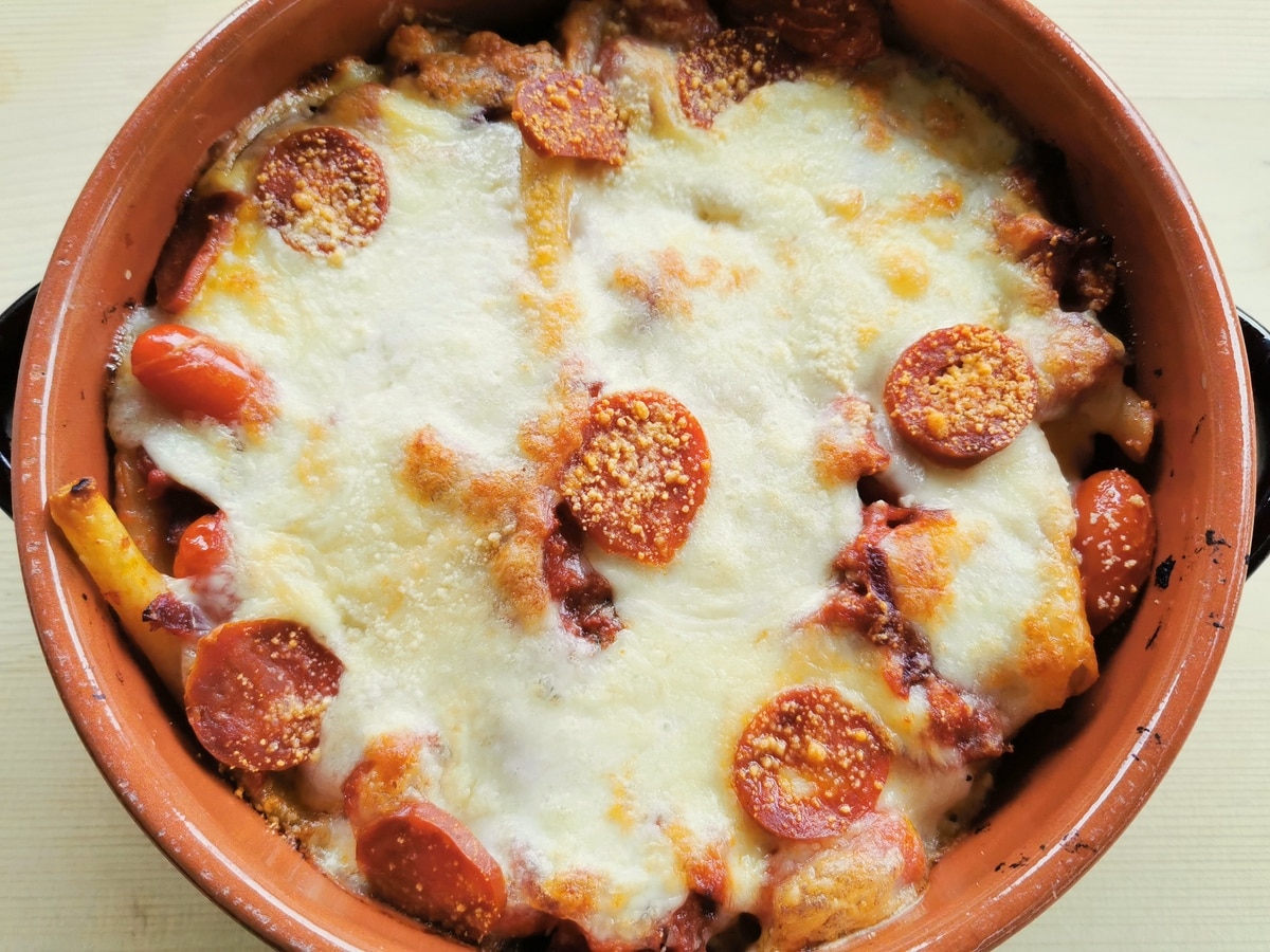 Baked ziti pasta with spicy sausage in a round terracotta oven dish..