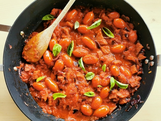 spicy sausage and onions in tomato sauce with basil in skillet