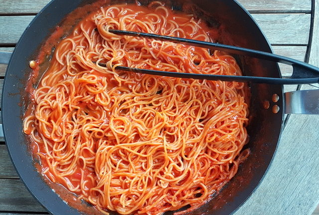 Spaghetti and tomato sauce cook together in the same pan