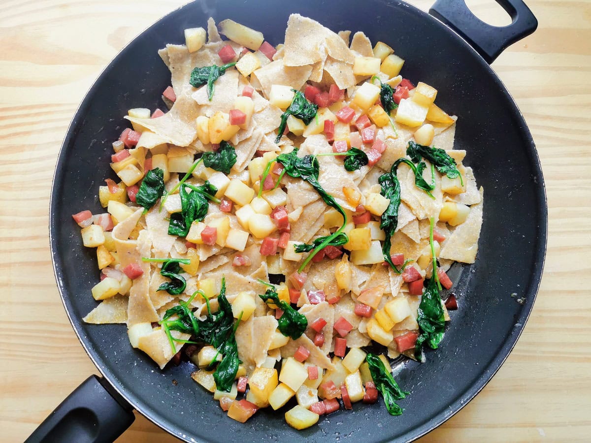 Cooked blecs pasta in large skillet with potatoes, speck and wilted spinach.