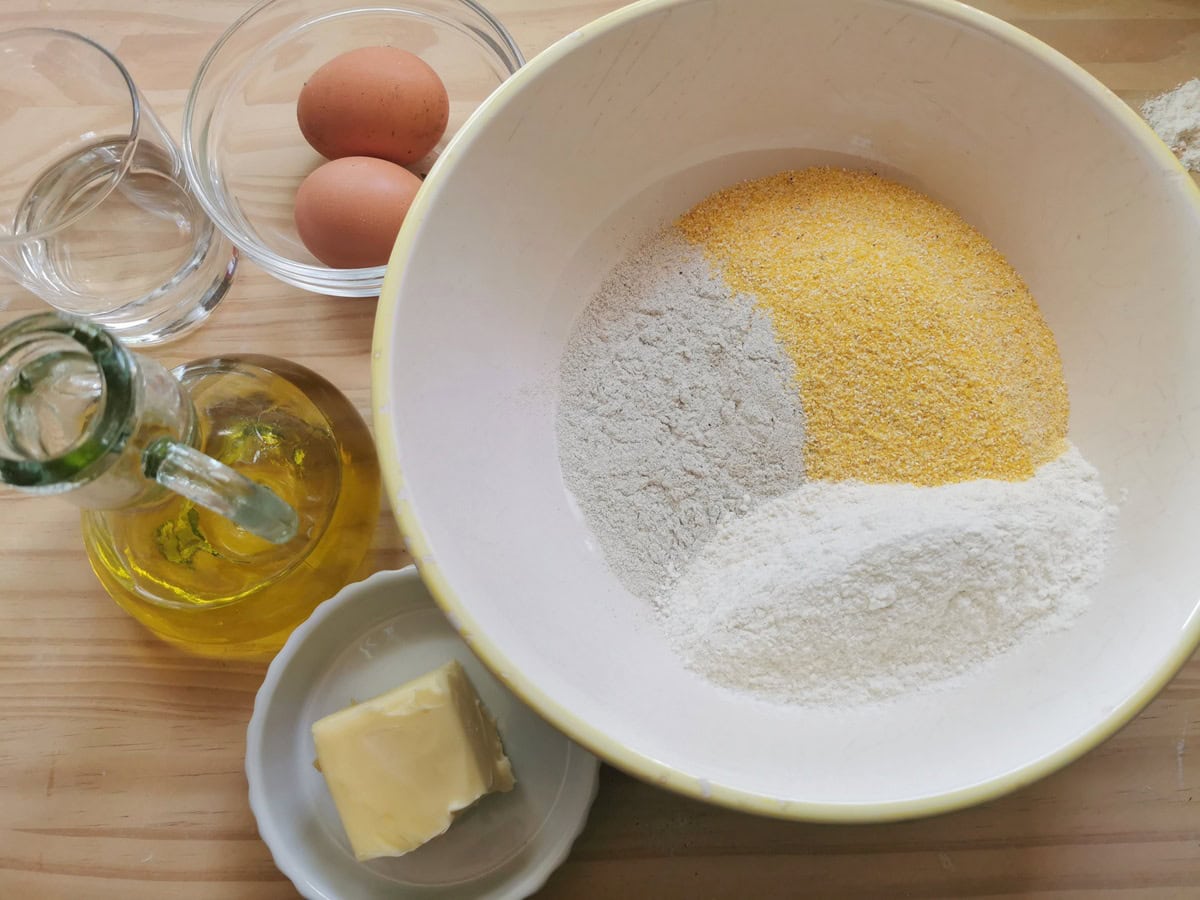 Ingredients for blecs pasta dough; 3 types of flour in a bowl, eggs, butter, olive oil and water.