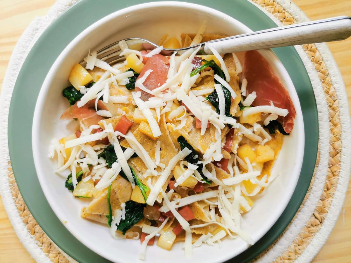 Blecs buckwheat pasta with potatoes and speck in bowl with grated montasio on top.