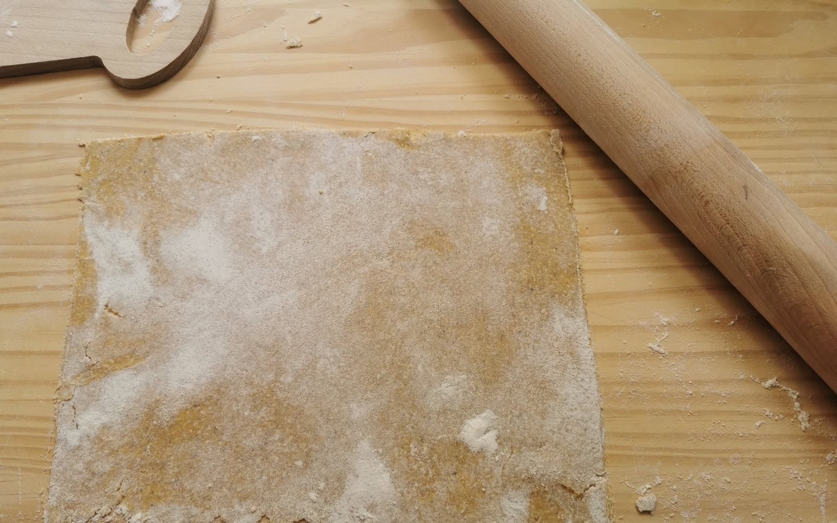 Sheet of rolled out blecs pasta dough on wood surface with rolling pin.