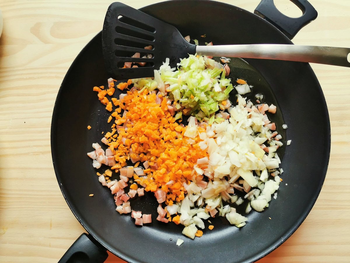 Chopped onion, celery amd carrots and pamcetta cubes cooking in skillet.