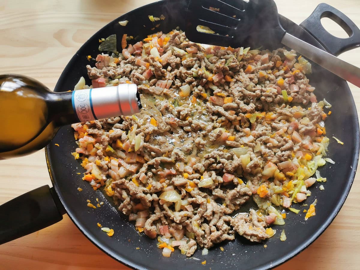 White wine being added to cooked ground beef and soffritto in skillet.