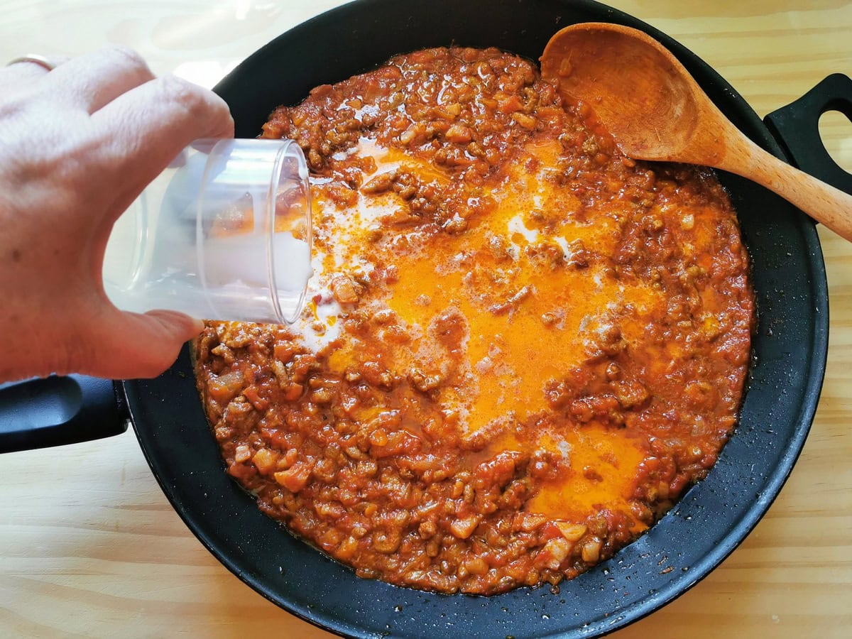 Milk being added to Bolognese sauce in skillet.