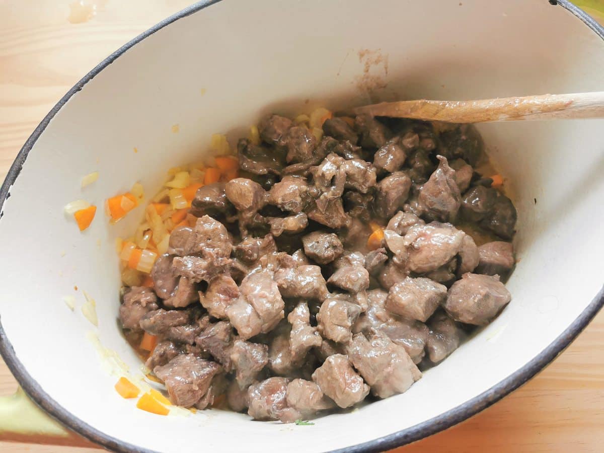 Browned hare pieces in Dutch oven with chopped vegetables.