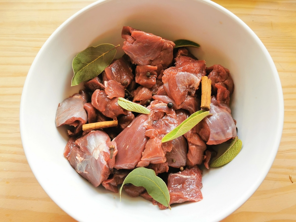 Uncooked pieces of hare Meat in white bowl with spices and herbs.