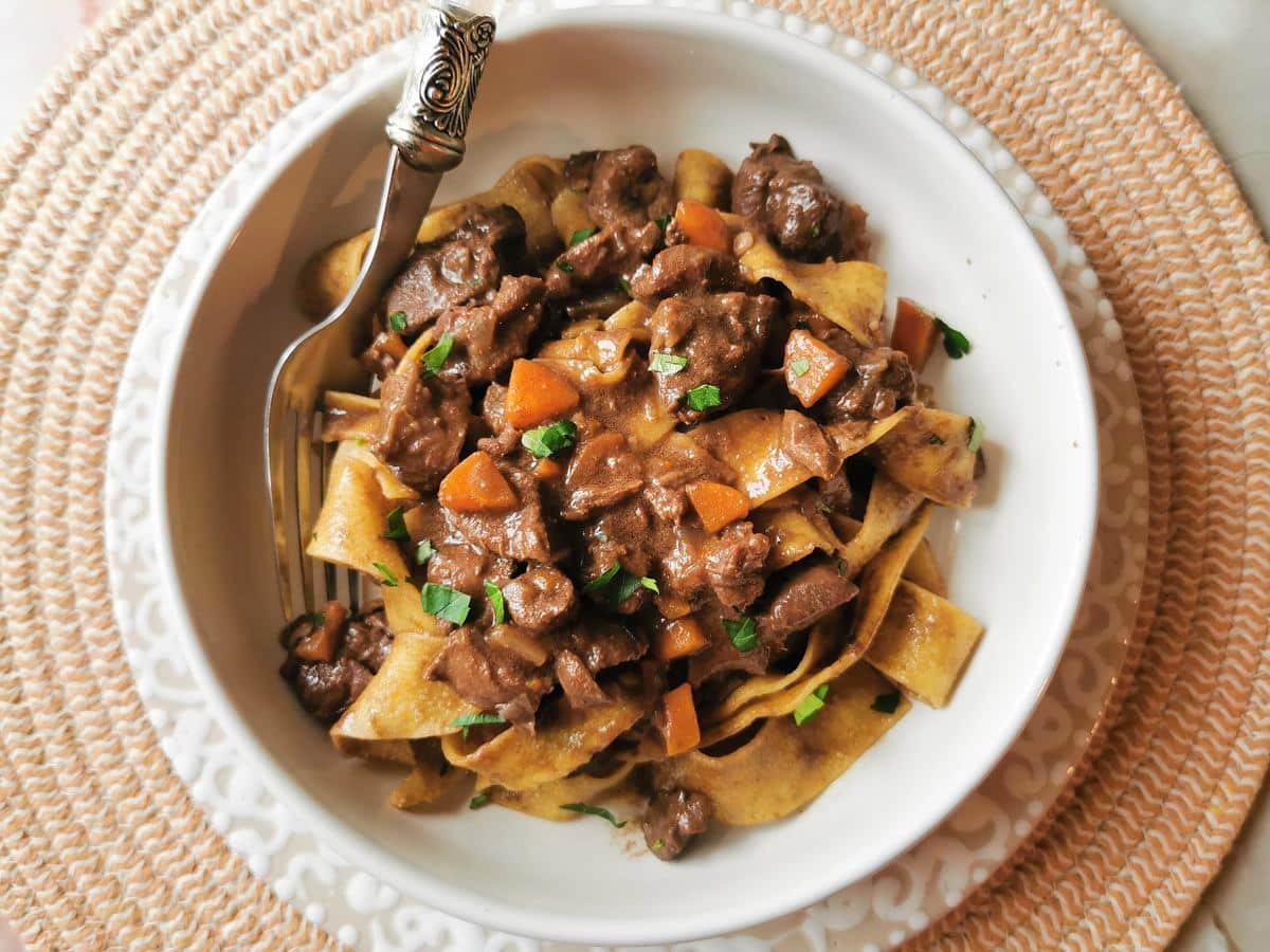 Braised hare ragu with pappardelle  in white bowl.