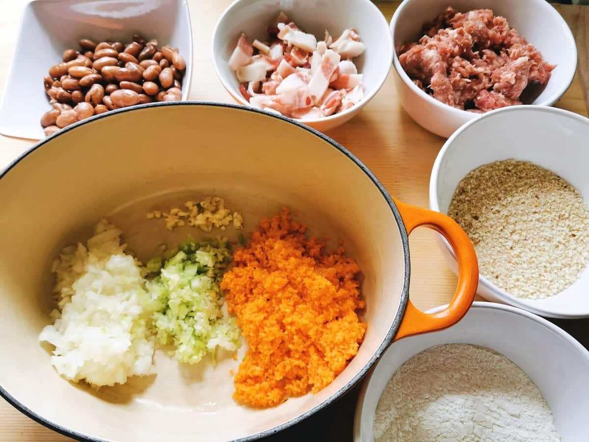 prepared ingredients for sausage and bean sauce with chopped onion, celery, carrots and garlic in Dutch oven.