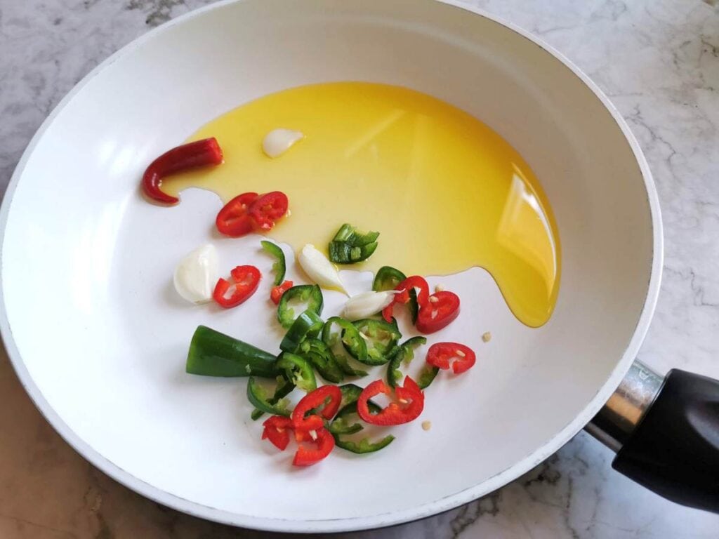 peeled garlic and chopped chilli peppers in frying pan with olive oil
