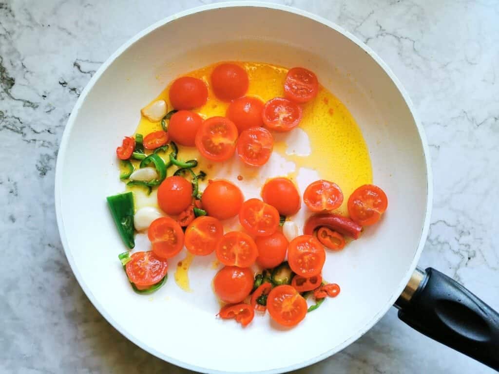 halved cherry tomatoes in frying pan with garlic and chilli peppers