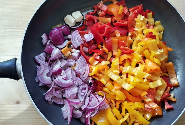 sliced red peppers, garlic cloves and red onions in a frying pan