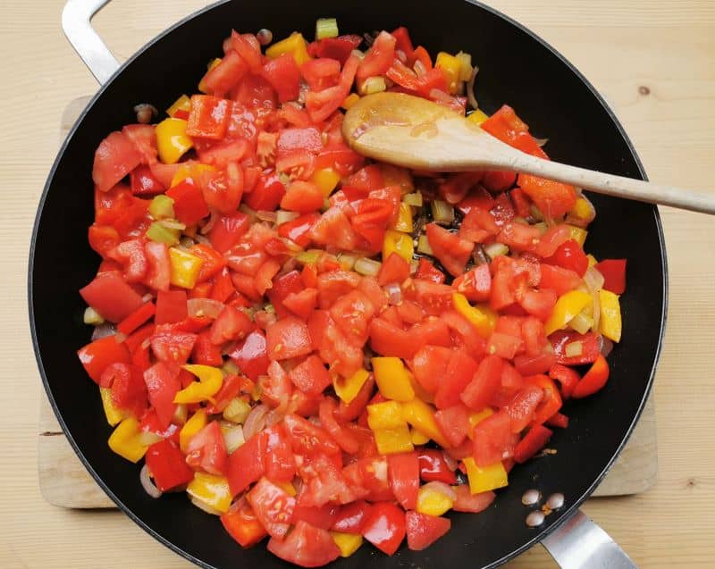 pieces of red and yellow peppers, onions, celery and peeled tomatoes in skillet