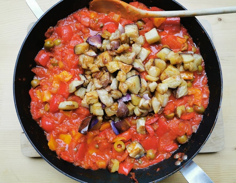 fried eggplant cubes added to caponata sauce in skillet