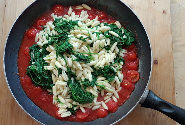 cavatelli pasta with rocket (arugula) in tomato sauce in frying pan