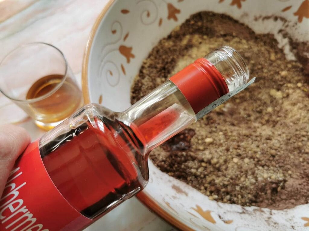 bottle of Alchermes liqueur held over bowl with chocolate and walnut mixture