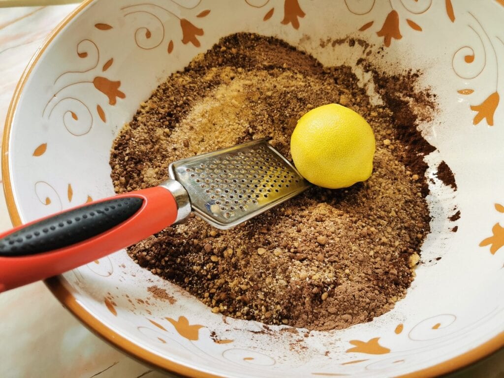 lemon and lemon grated in bowl with breadcrums, walnuts, sugar and cocoa.