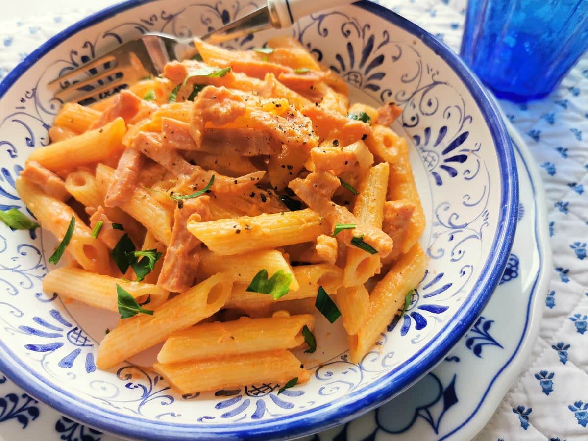 Creamy ham and tomato penne pasta in a bowl.