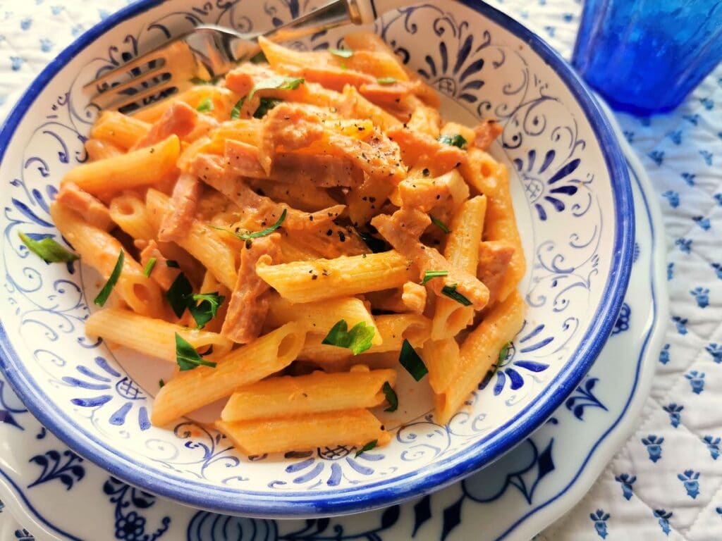 Creamy ham and tomato penne al baffo served on a kitchen table.