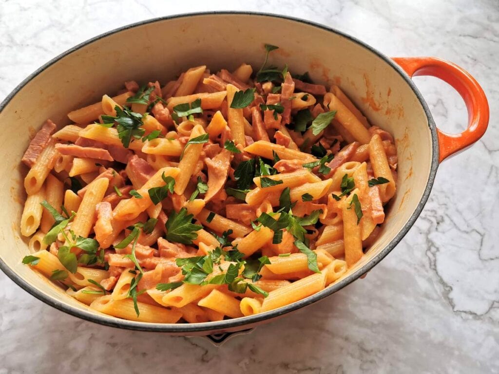 Creamy ham and tomato penne al baffo garnished with parsley.