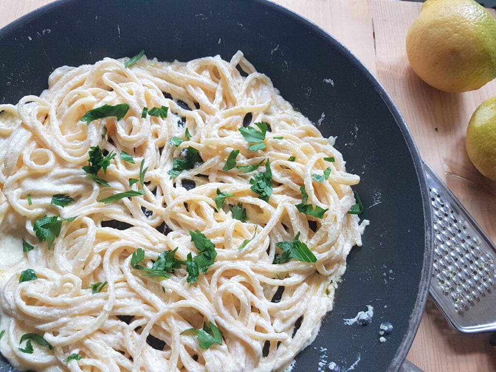 cooked pasta mixed with creamy lemon sauce in pan with added chopped parsley