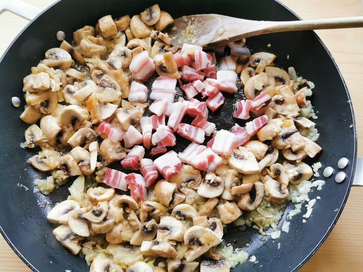 Chopped pancetta in skillet with mushrooms and onions.