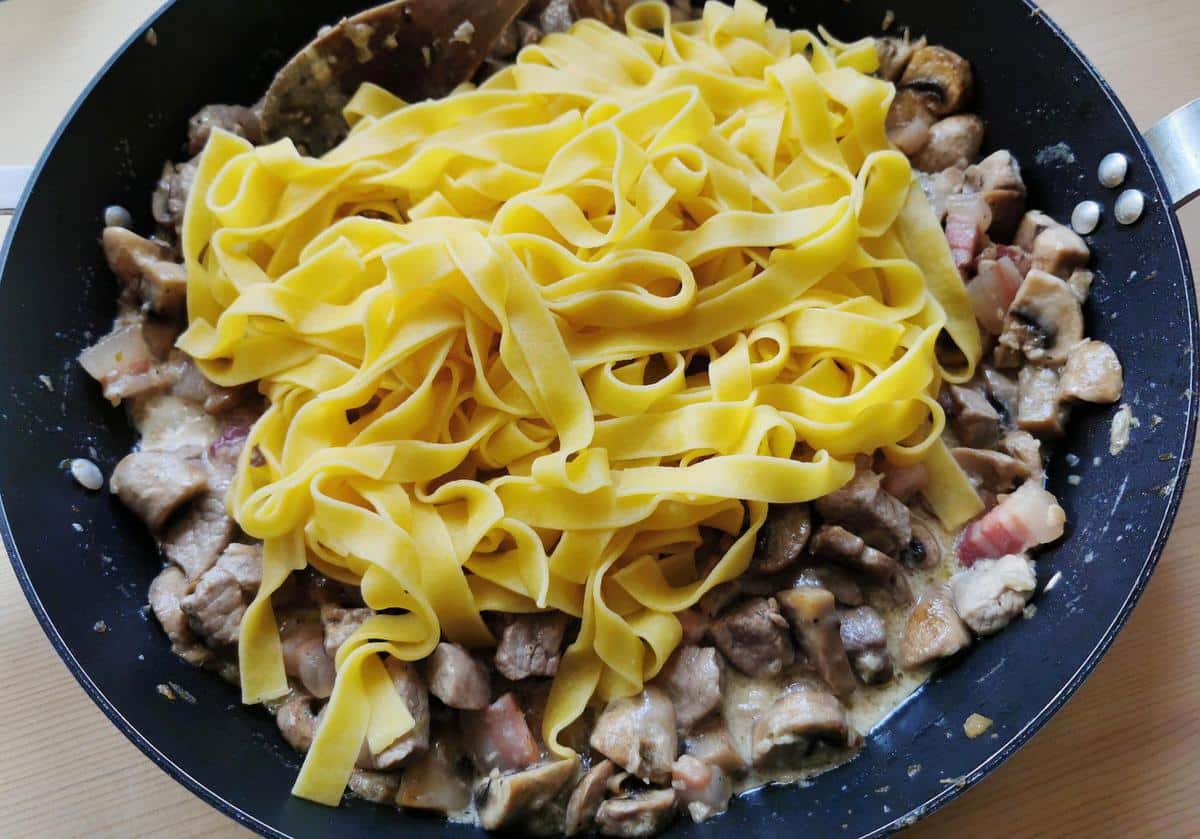 Cooked tagliatelle added to pork tenderloin sauce in skillet.