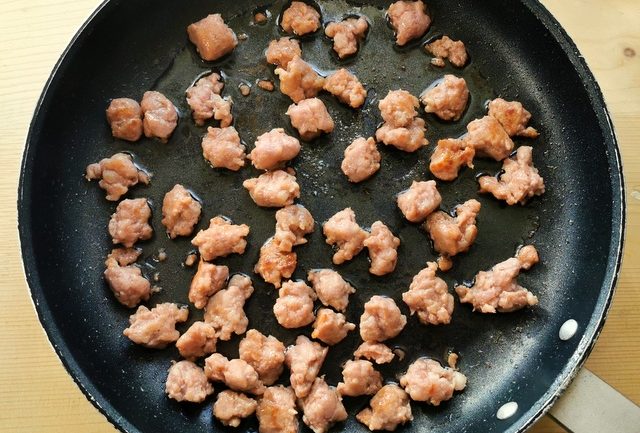 luganega sausage pieces cooking in frying pan