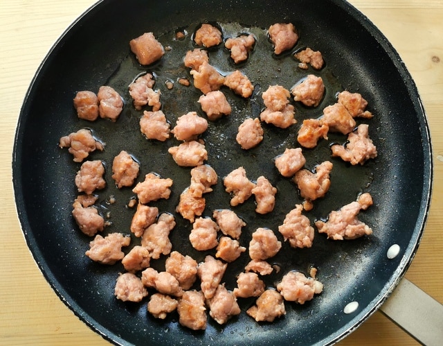 luganega sausage pieces cooking in frying pan