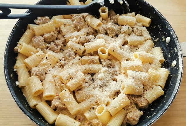 grated grana cheese added to pasta and sausage sauce in frying pan