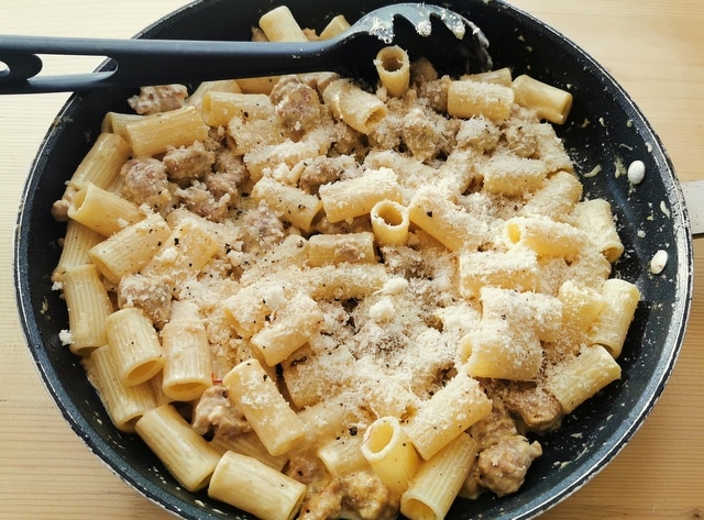 grated grana cheese added to pasta and sausage sauce in frying pan