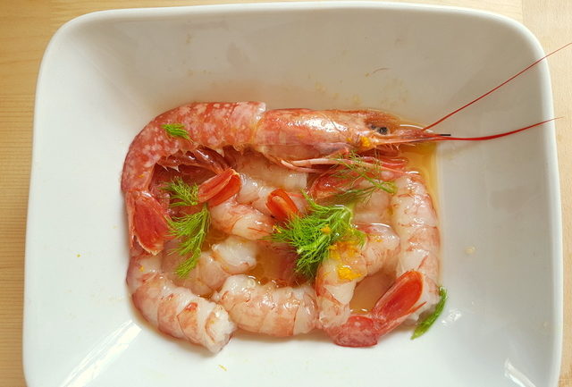 raw prawns marinating in orange juice in white bowl 