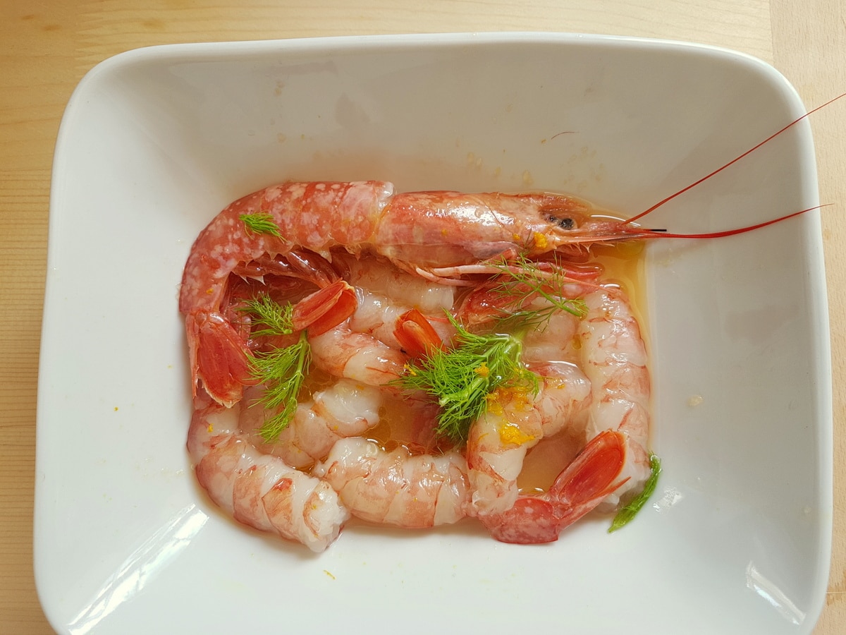 Prawns, orange zest, orange juice, olive oil and fennel greens in a bowl.