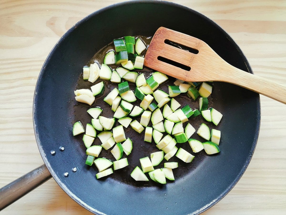 zucchini pieces and garlic cloves cooking in skillet