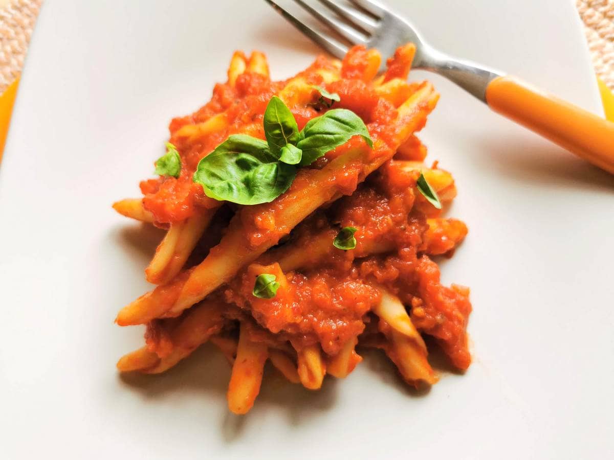 A portion of fileja pasta with nduja on a square white plate.