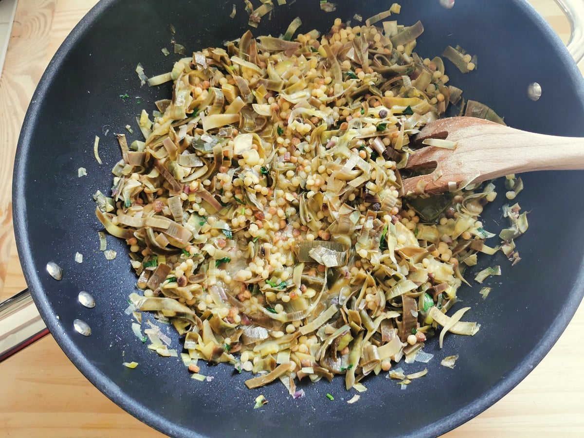 Fregola pasta with artichokes cooking in deep frying pan.