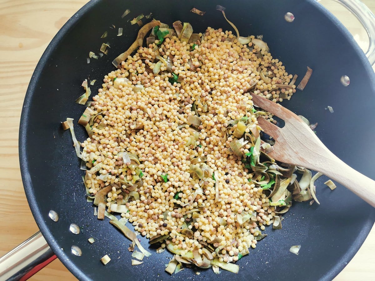 Toasted fregola in deep frying pan with artichokes and leek.