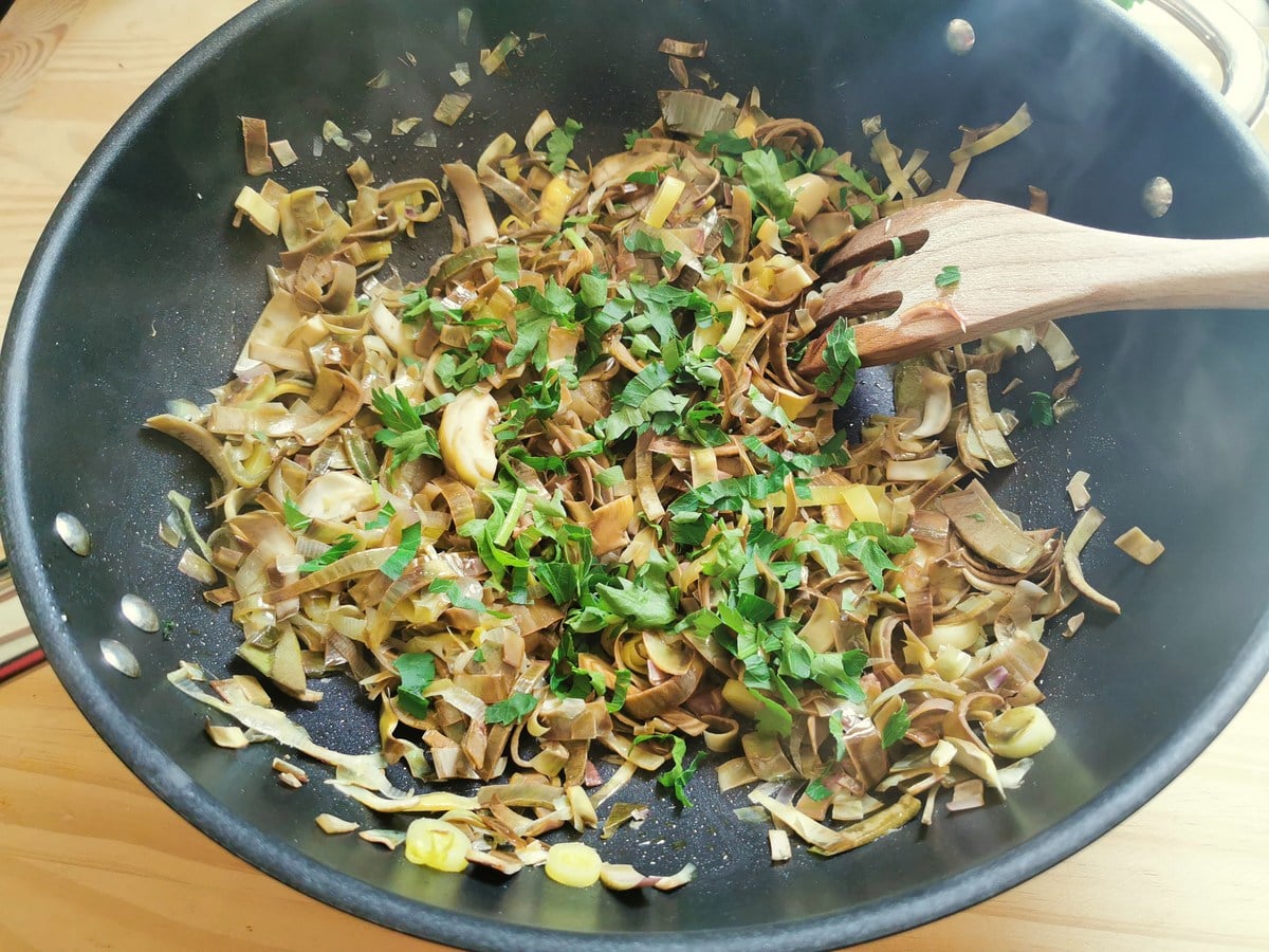 Chopped fresh parsley and garlic added to deep frying pan with artichokes.