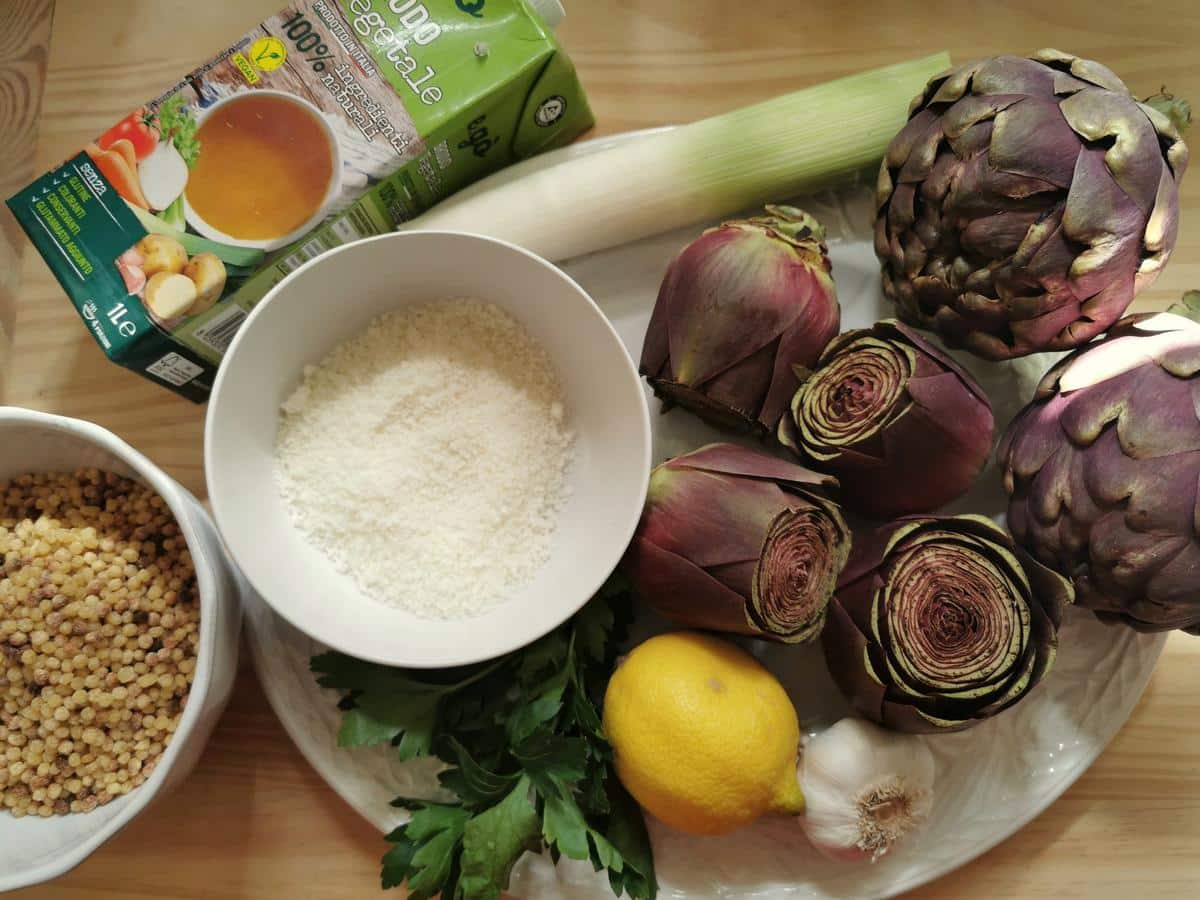 Ingredients for fregola with artichokes on white plate.