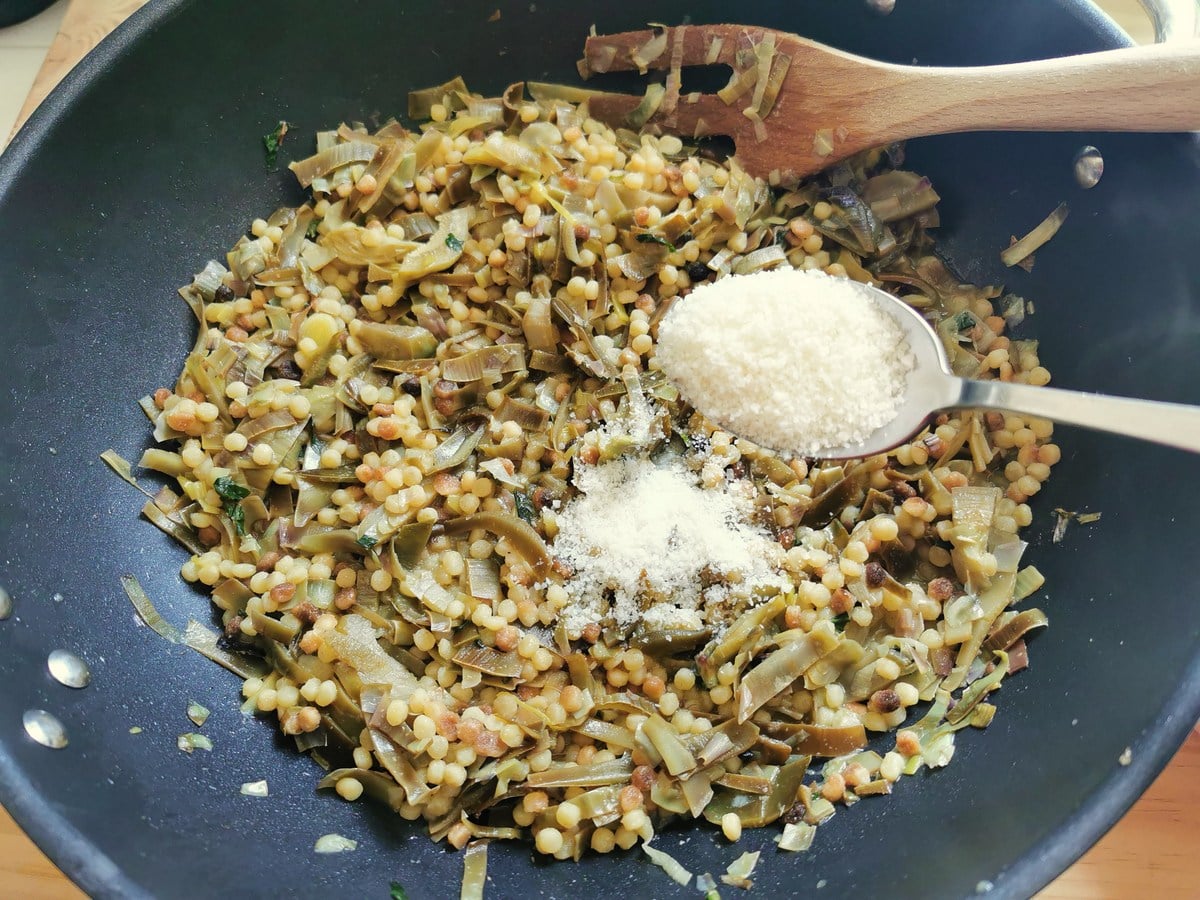 Tablespoons of grated Pecorino added to the pasta and artichokes in deep frying pan.