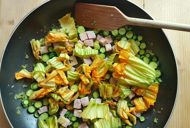 onion, zucchini, chopped ham and zucchini flowers in frying pan