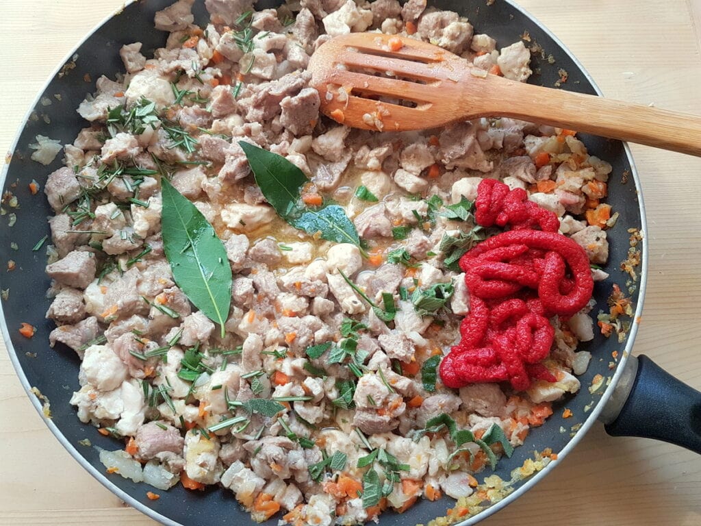 mixed meats and veggies cooking in skillet with tomato concentrate and herbs