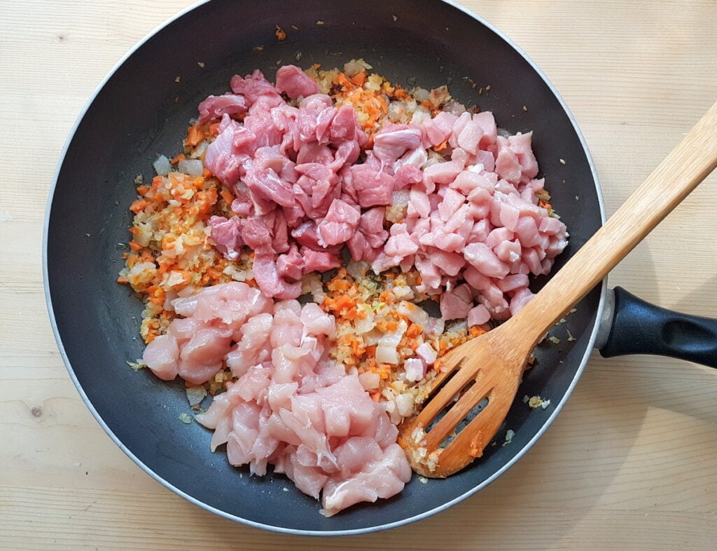 chicken, pork and veal pieces in skillet with carrots, onions and lardo