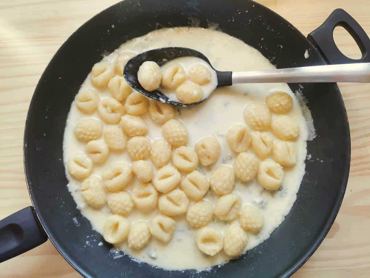 Gnocchi mixed with the Gorgonzola sauce in a skillet.