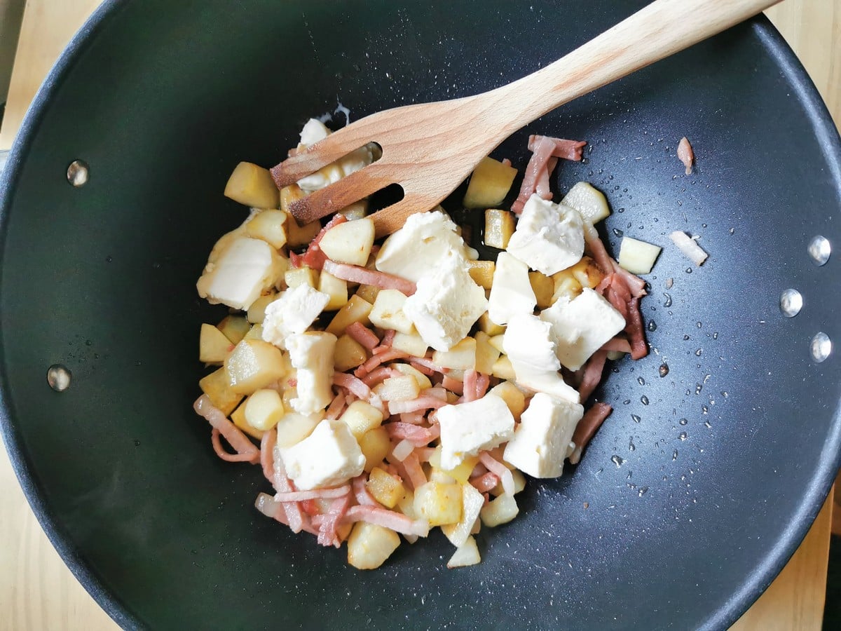 Pieces of taleggio added to deep frying pan with pears and speck.