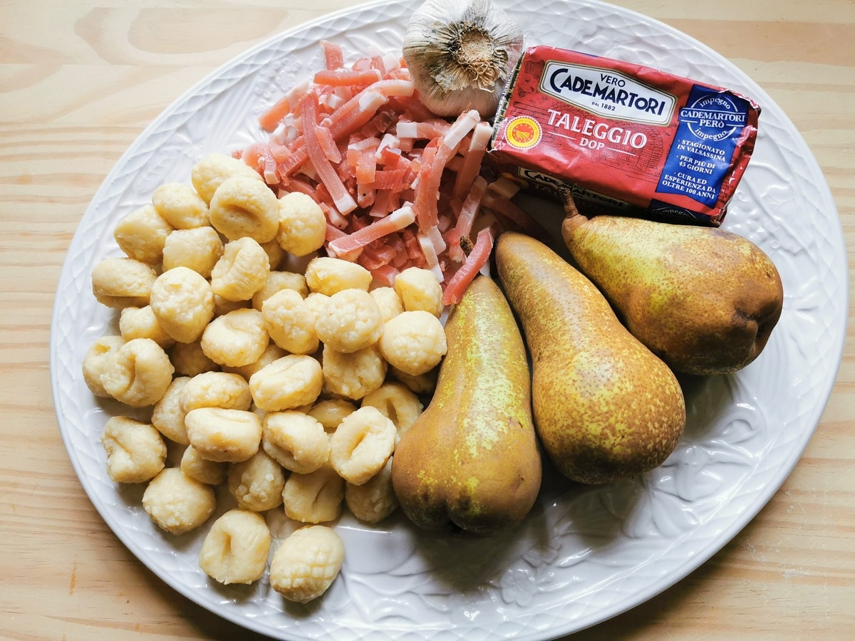 Ingredients for gnocchi with taleggio, pears and speck on white plate.