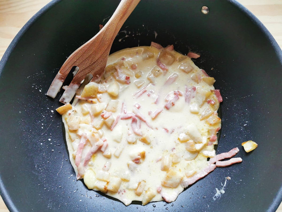 Ready taleggio sauce in deep frying pan with pieces of pear and speck.