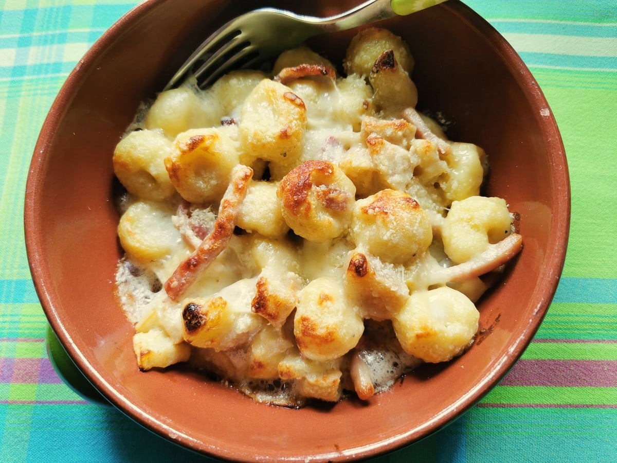 Baked gnocchi with taleggio, pears and speck in an earthenware bowl.