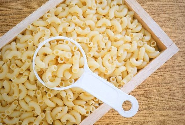 uncooked and dried elbow macaroni or gomiti elbow pasta in plastic measuring cup.